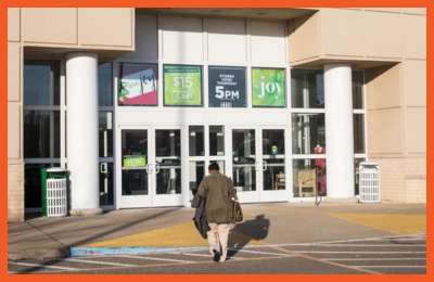 A customer walks toward the entrance of Black Friday Deals – Memphis, with promotional signs displaying store hours and seasonal discounts on the glass doors.