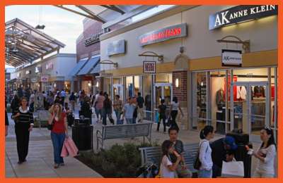 Shoppers walk through a busy outlet mall with brand stores like Anne Klein and Lucky Brand Jeans, enjoying the Best Friday Deals – Houston.